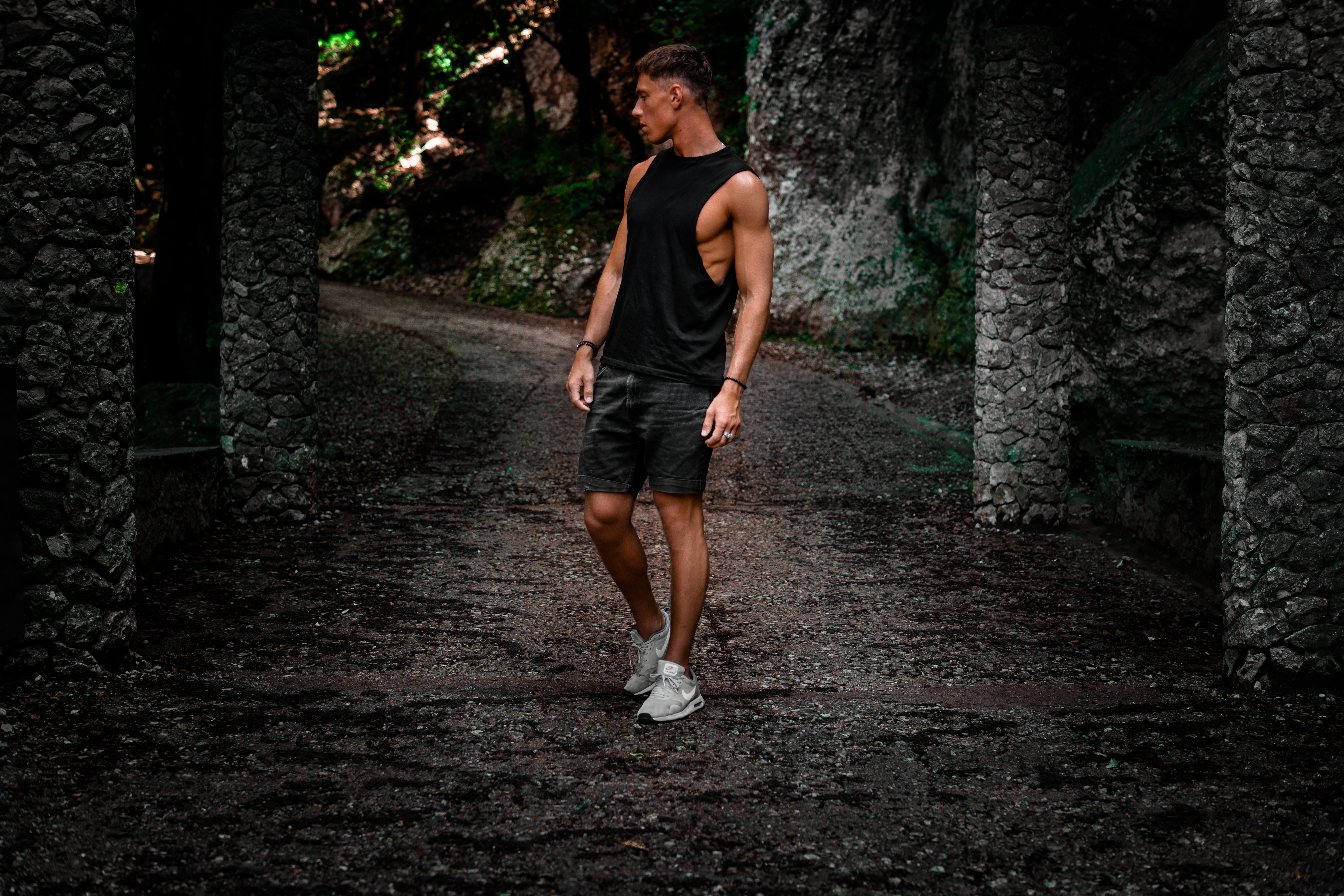 man standing on pathway between concrete post, tree, full length