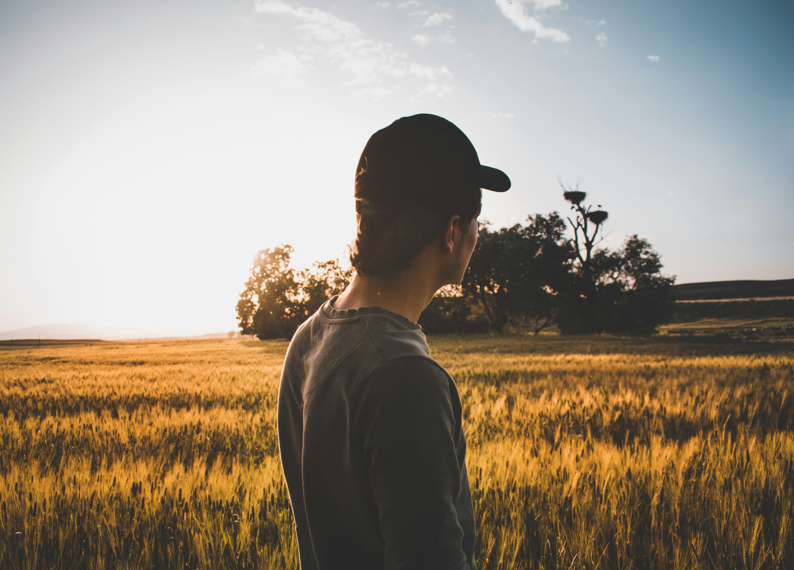 man with fitted cap facing brown grass field, sky, one person