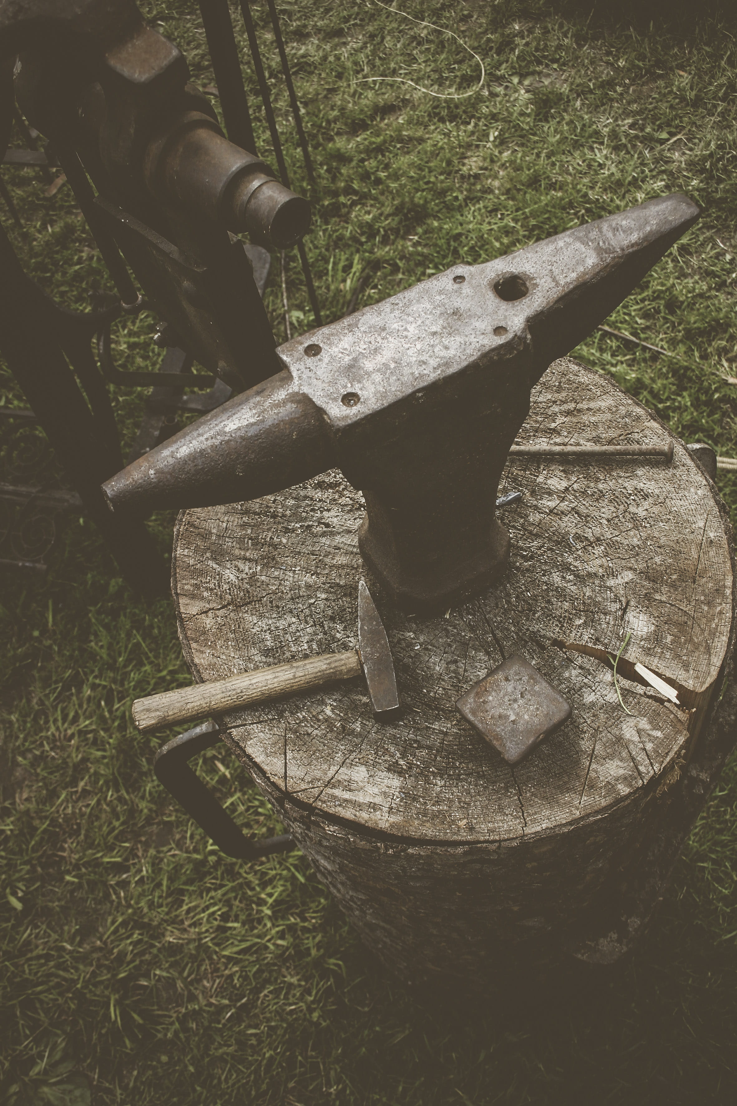 metal anvil on cut log with hammers, no people, grass, old, rusty