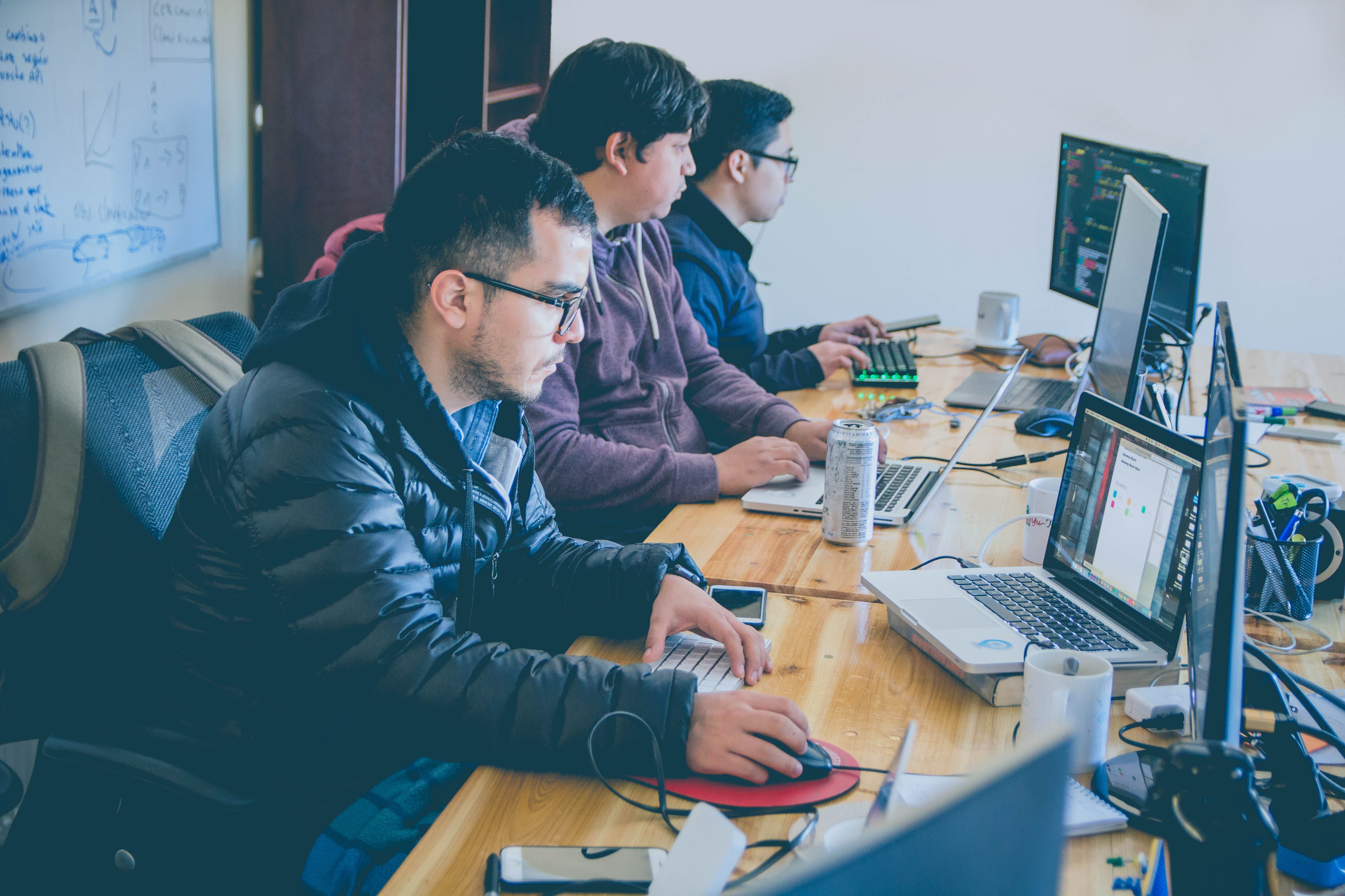 three men facing computer monitors, table, sitting, communication