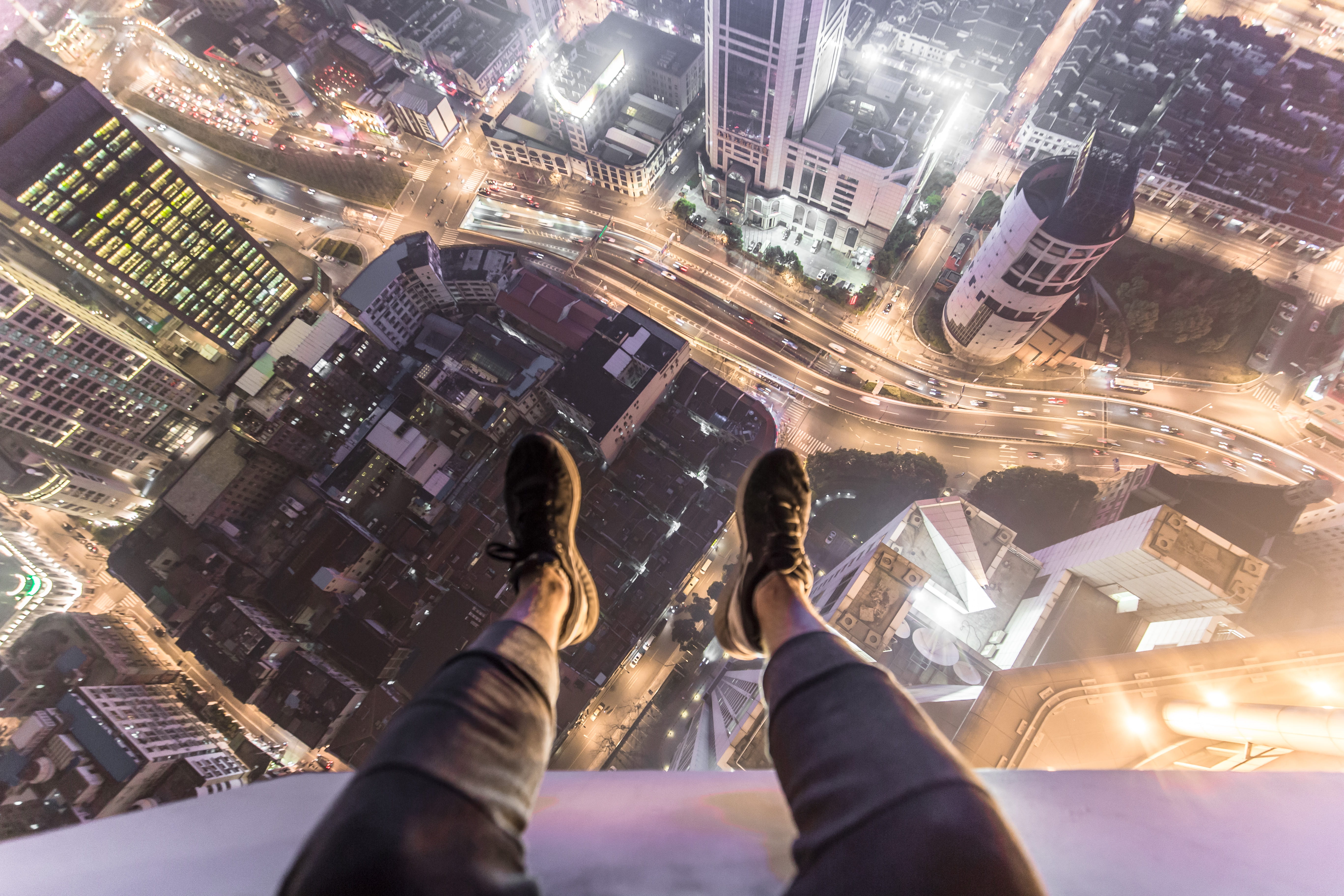 A person sitting on top of a skyscraper and dangling their legs over the edge.