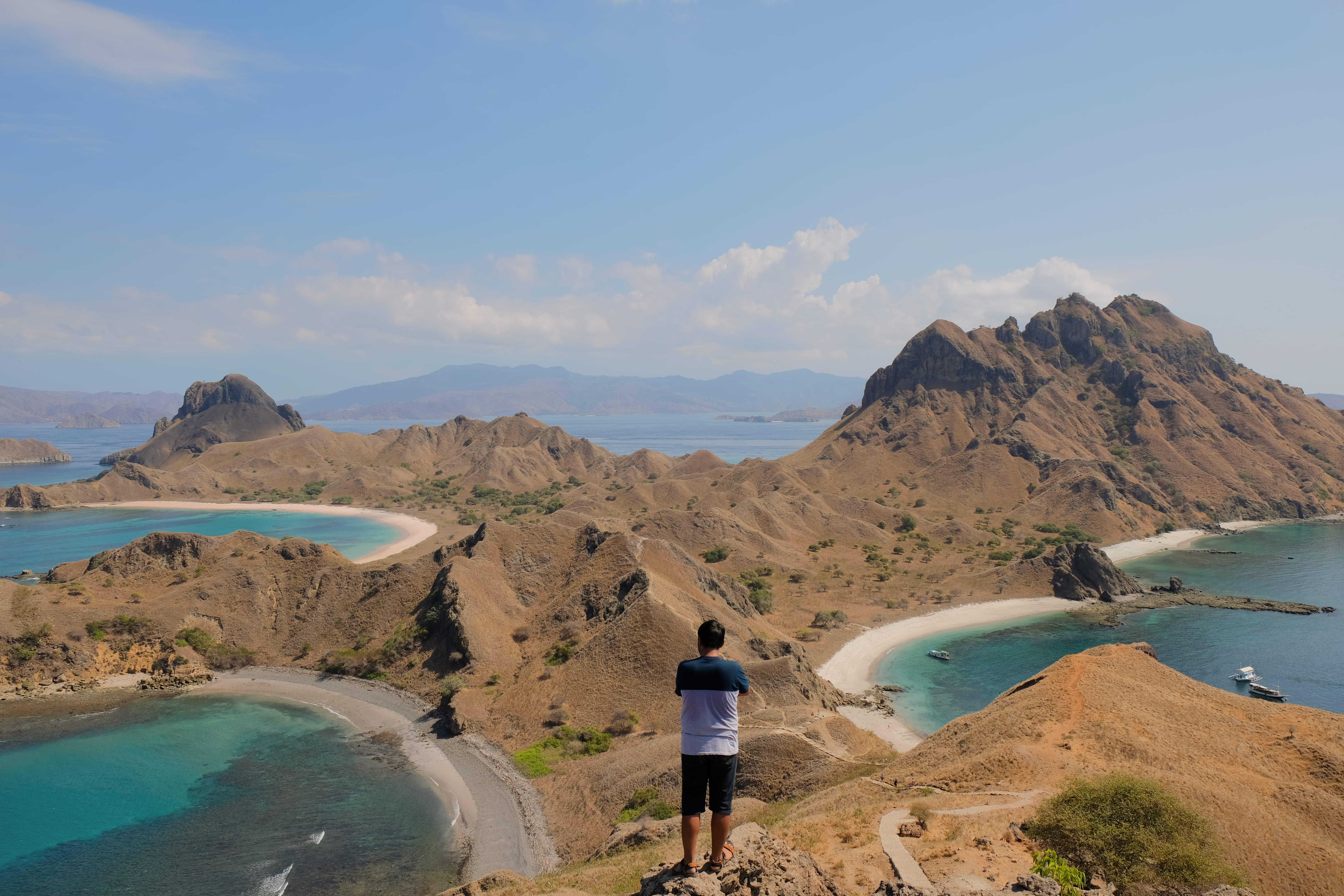man in blue and white shirt standing on cliff, promontory, padar island