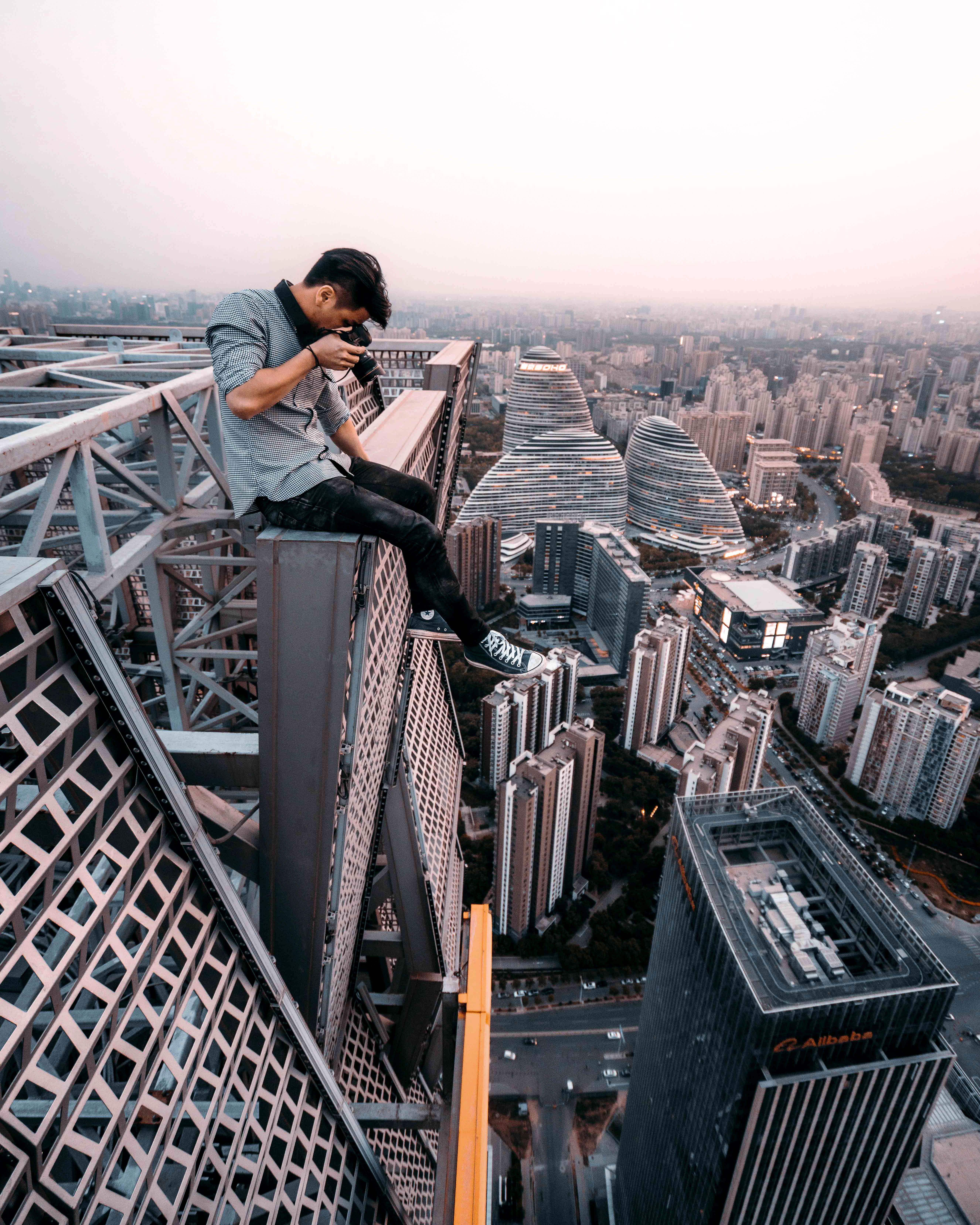man sitting on top of building taking photo below, extreme, dangerous