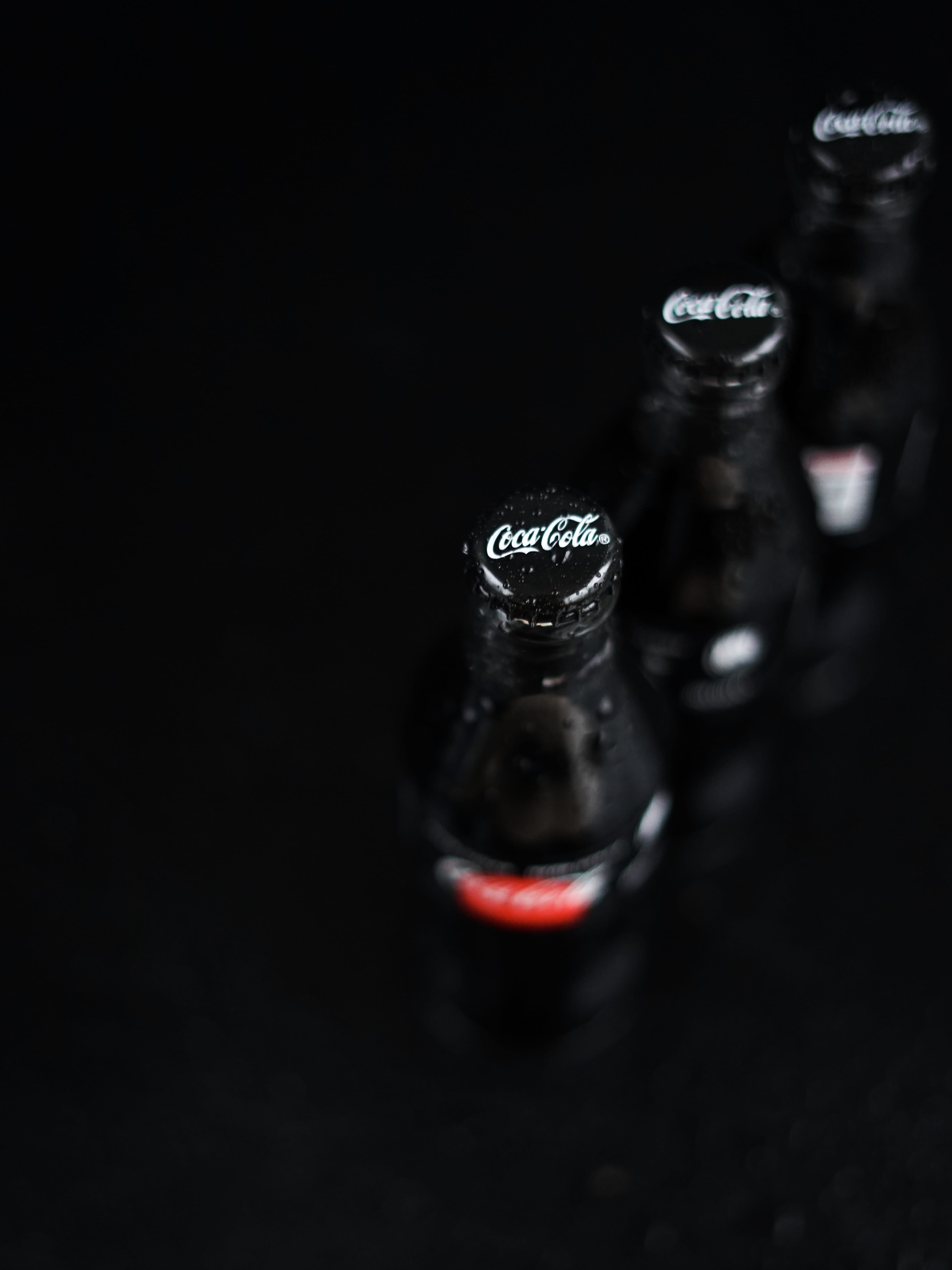 three Coca-Cola bottles, black background, studio shot, indoors