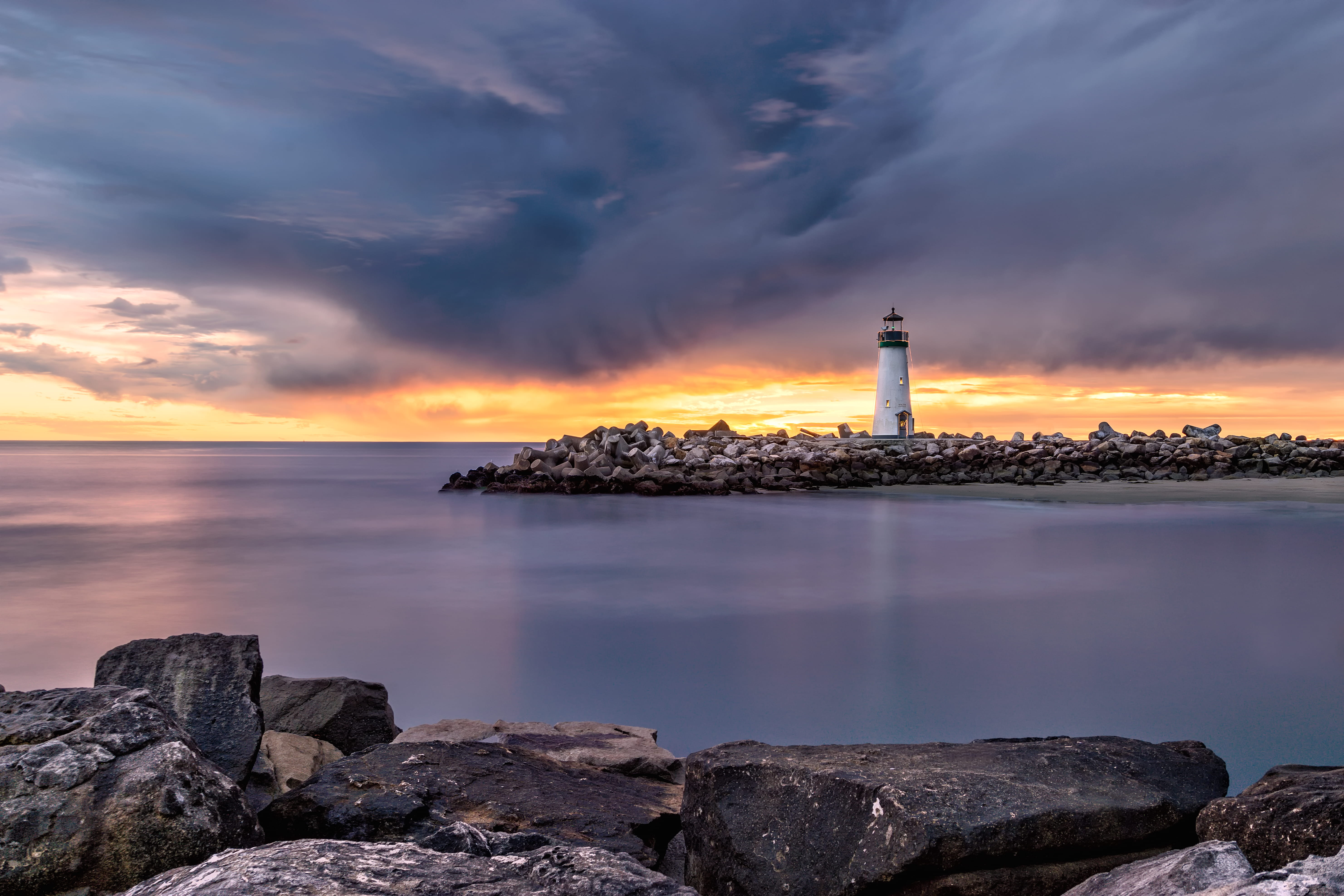 white lighthouse on shore beside body of water, breakwater, sunrise