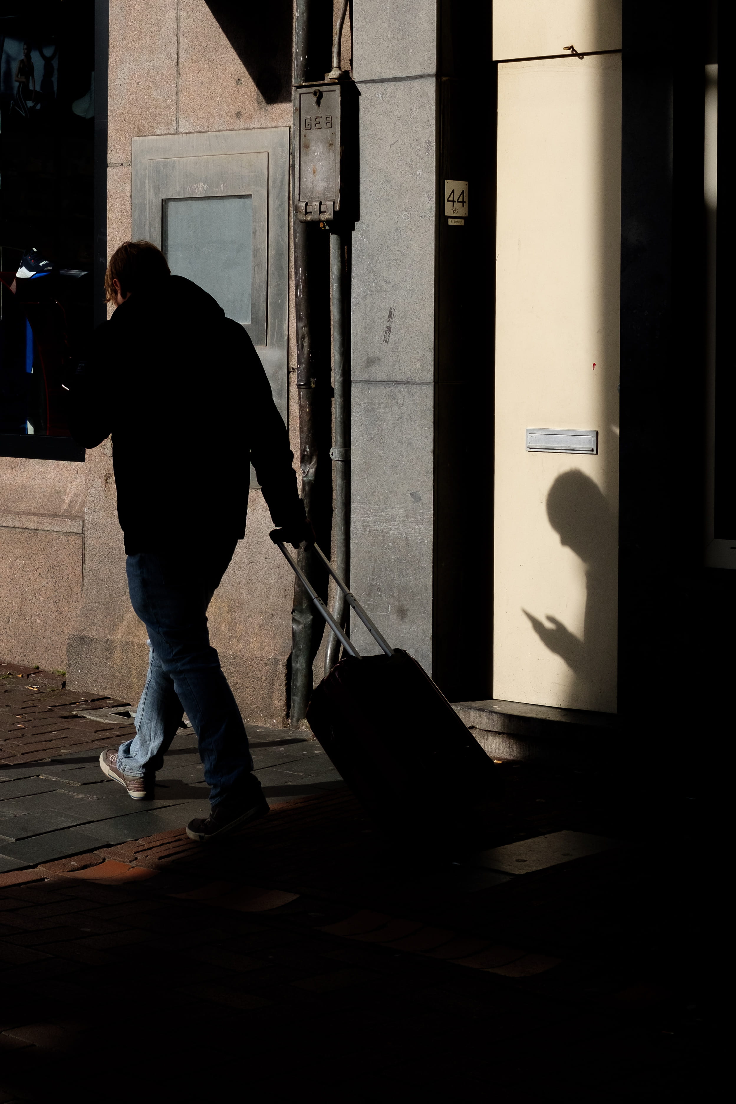 man walking on sidewalk while pulling luggage at night-time, human