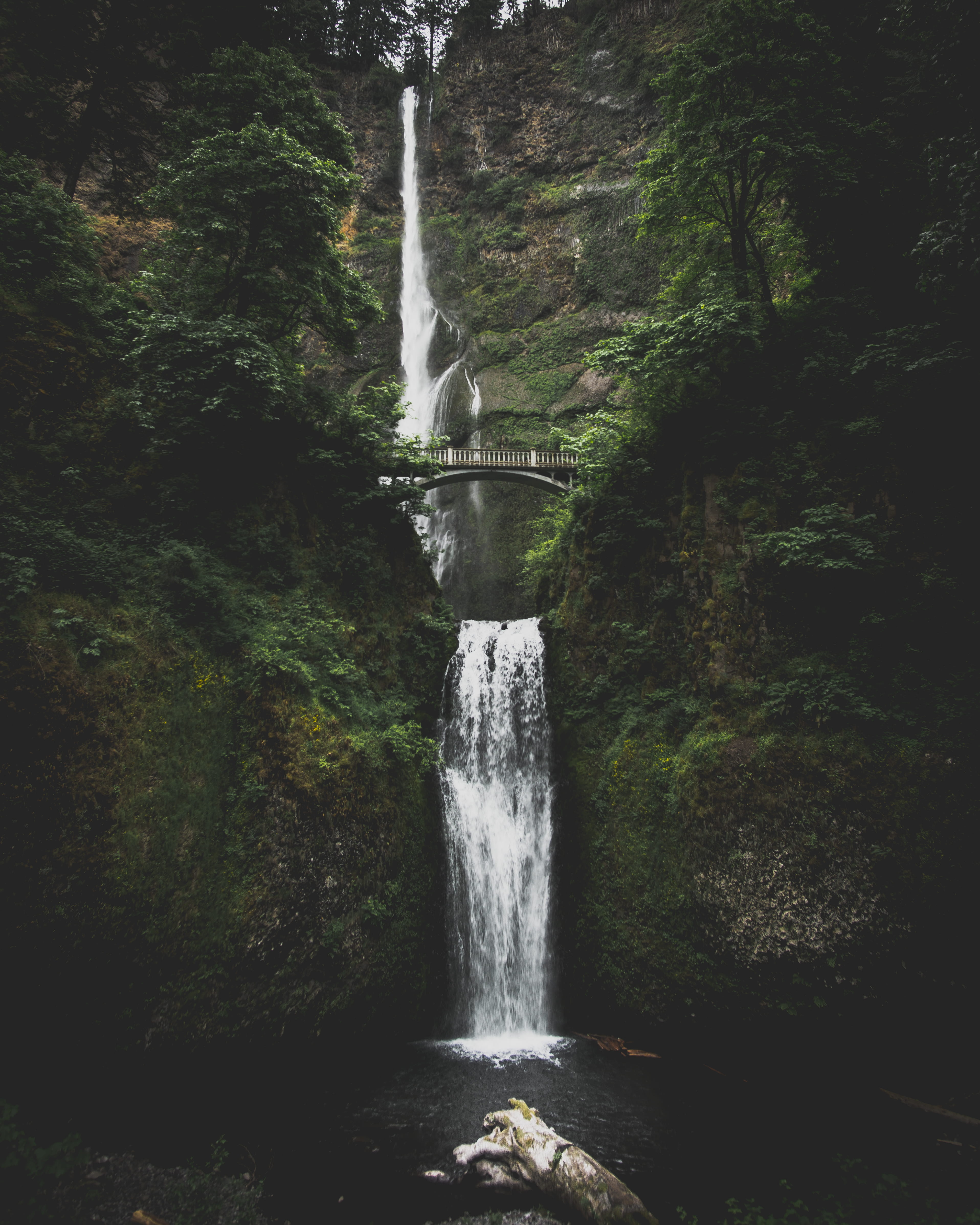 waterfall in between mountains with bridge, river, stream, tree