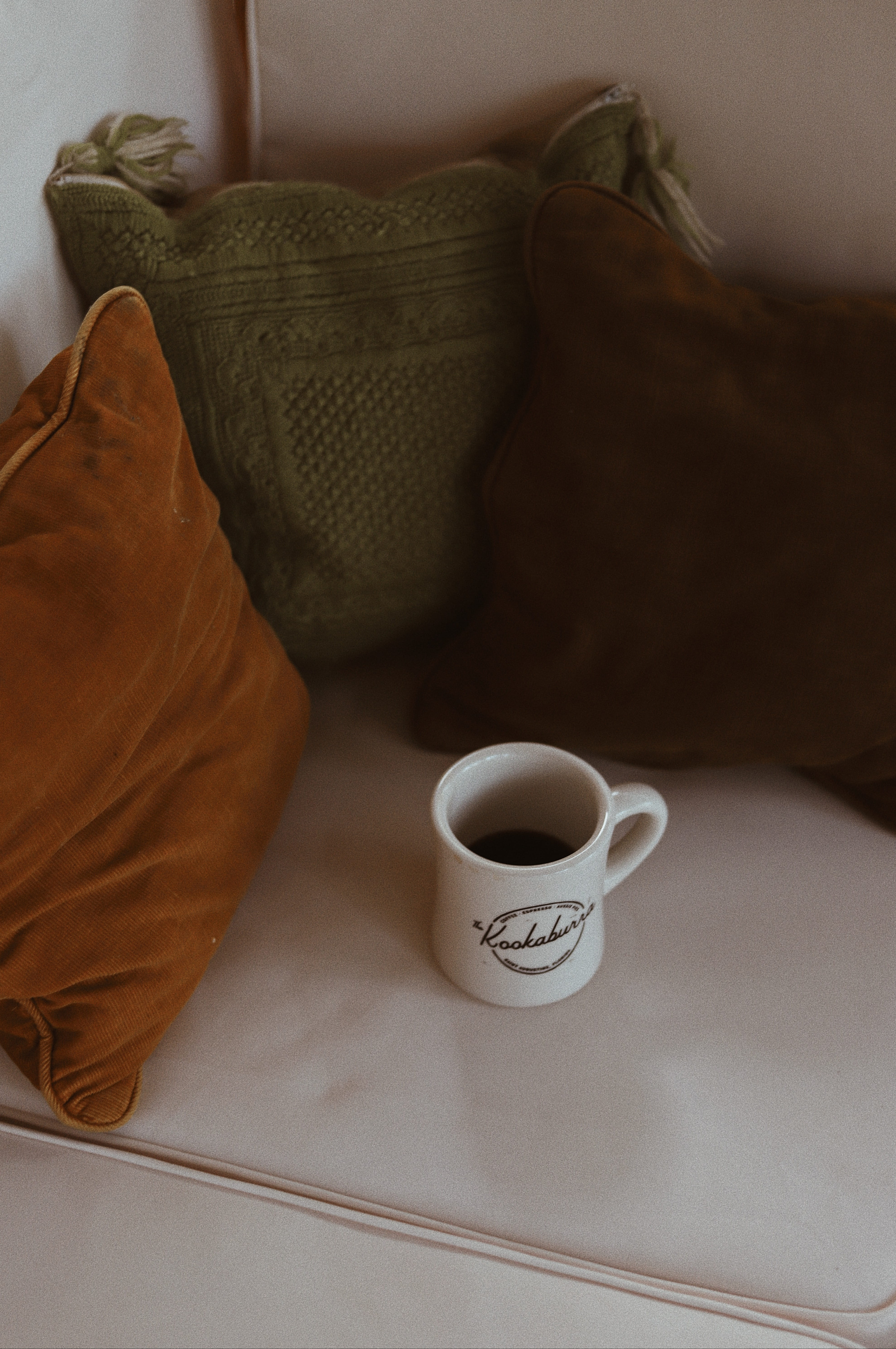 white ceramic mug near three assorted-color throw pillows, cup