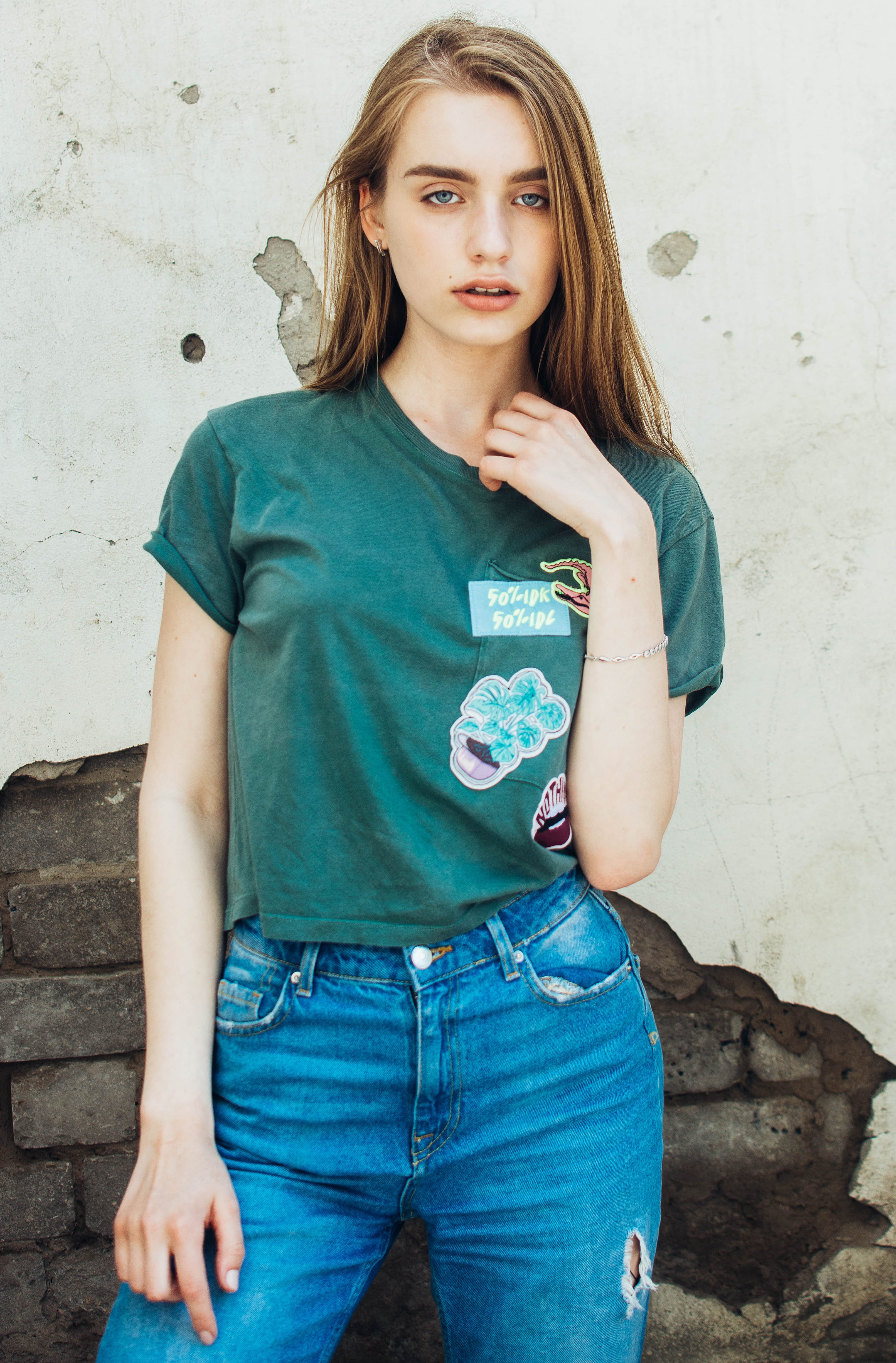 woman wearing green crew-neck t-shirt and blue jeans standing beside wall