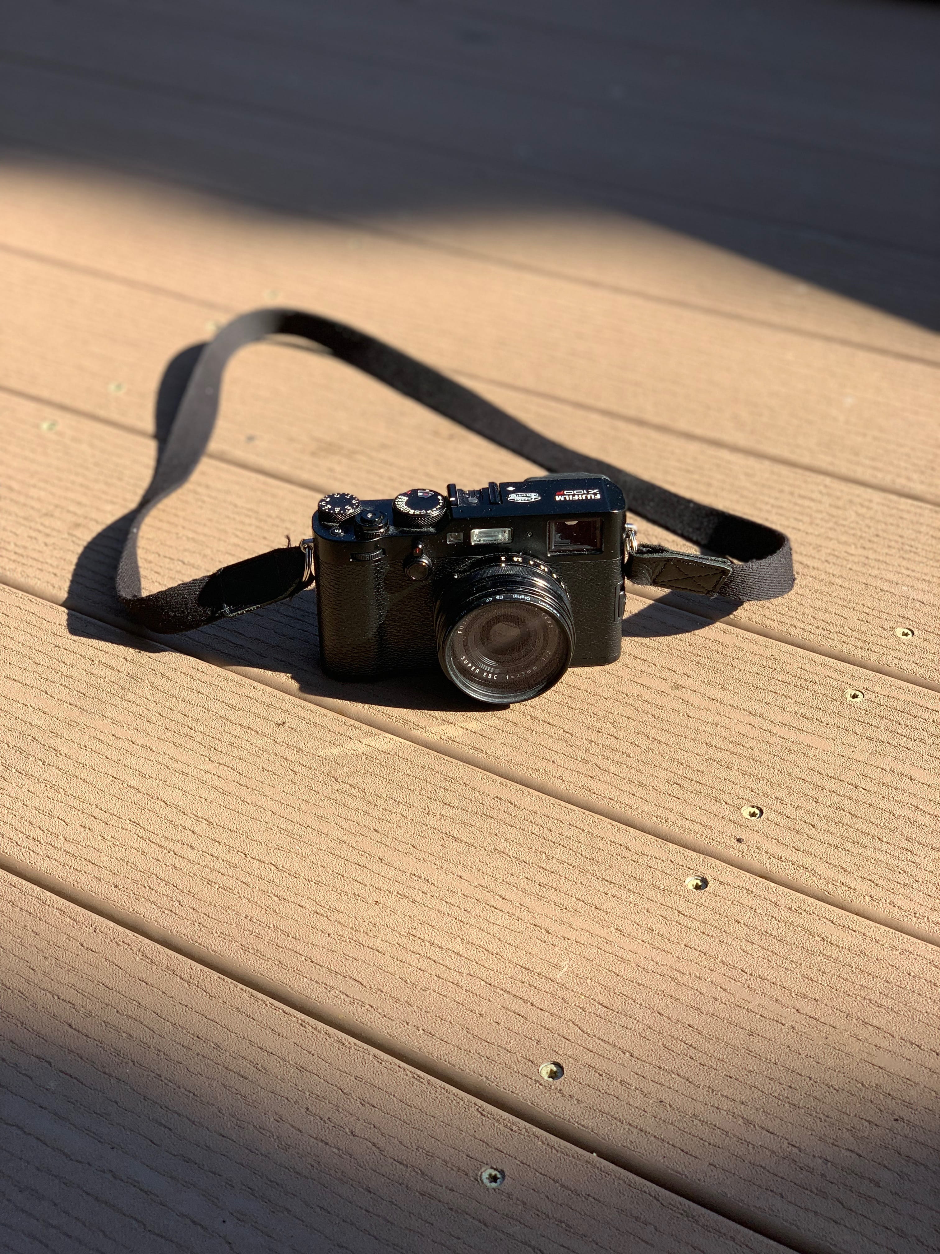 black SLR camera with strap on brown surface, electronics, wood