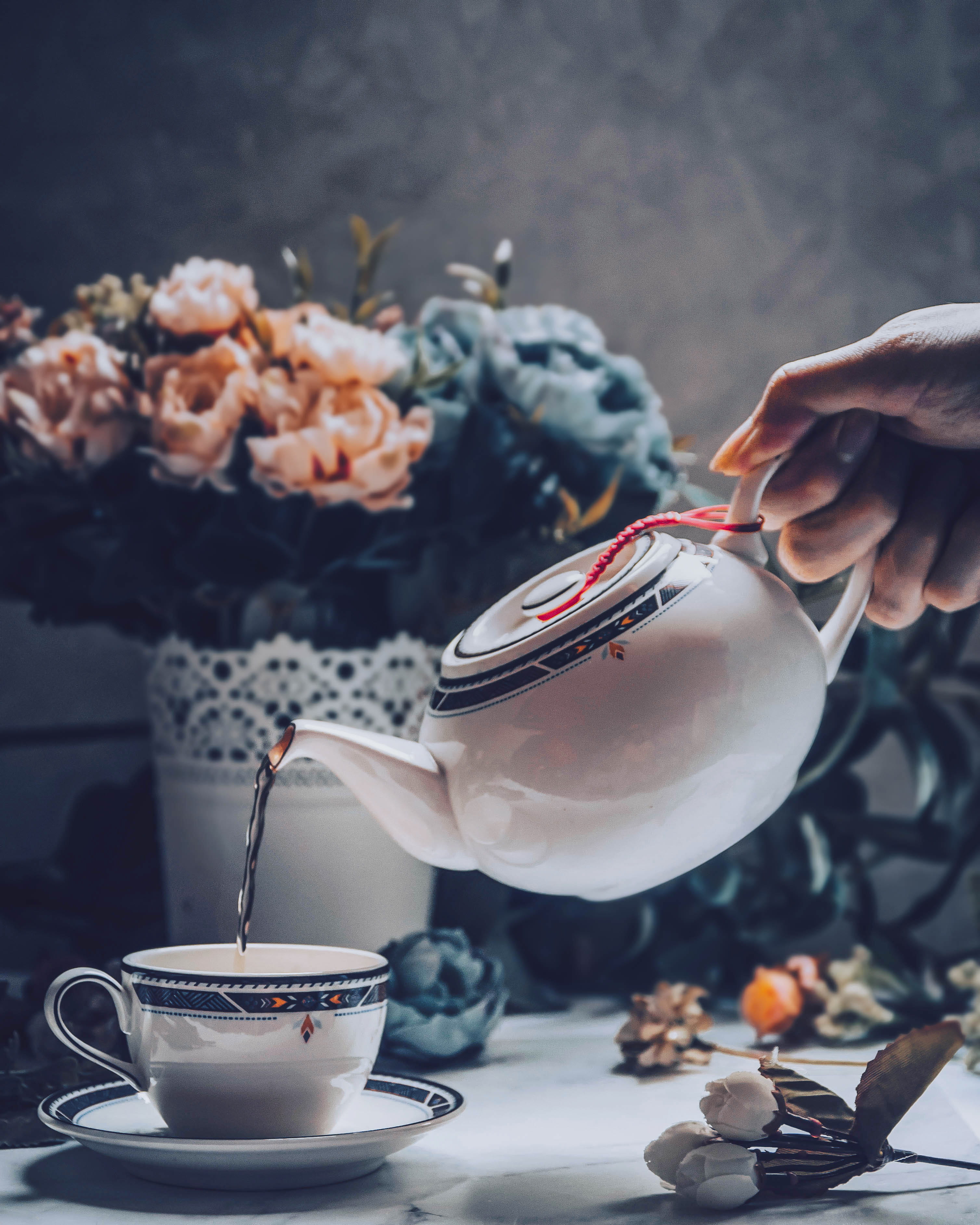 person holding white ceramic teapot, cup, flower, plant, vase