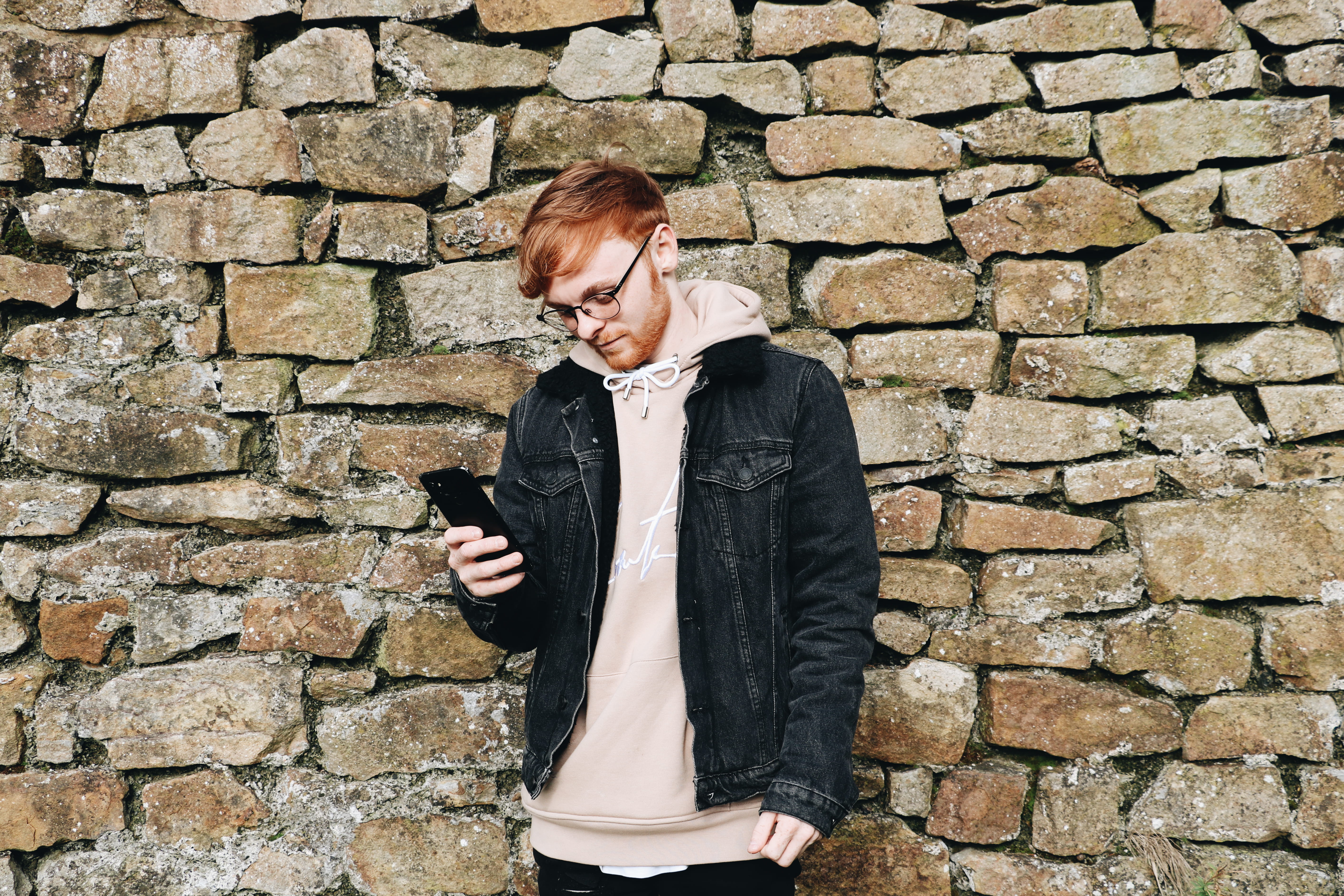 man looking down while holding smartphone, wall, coat, jacket