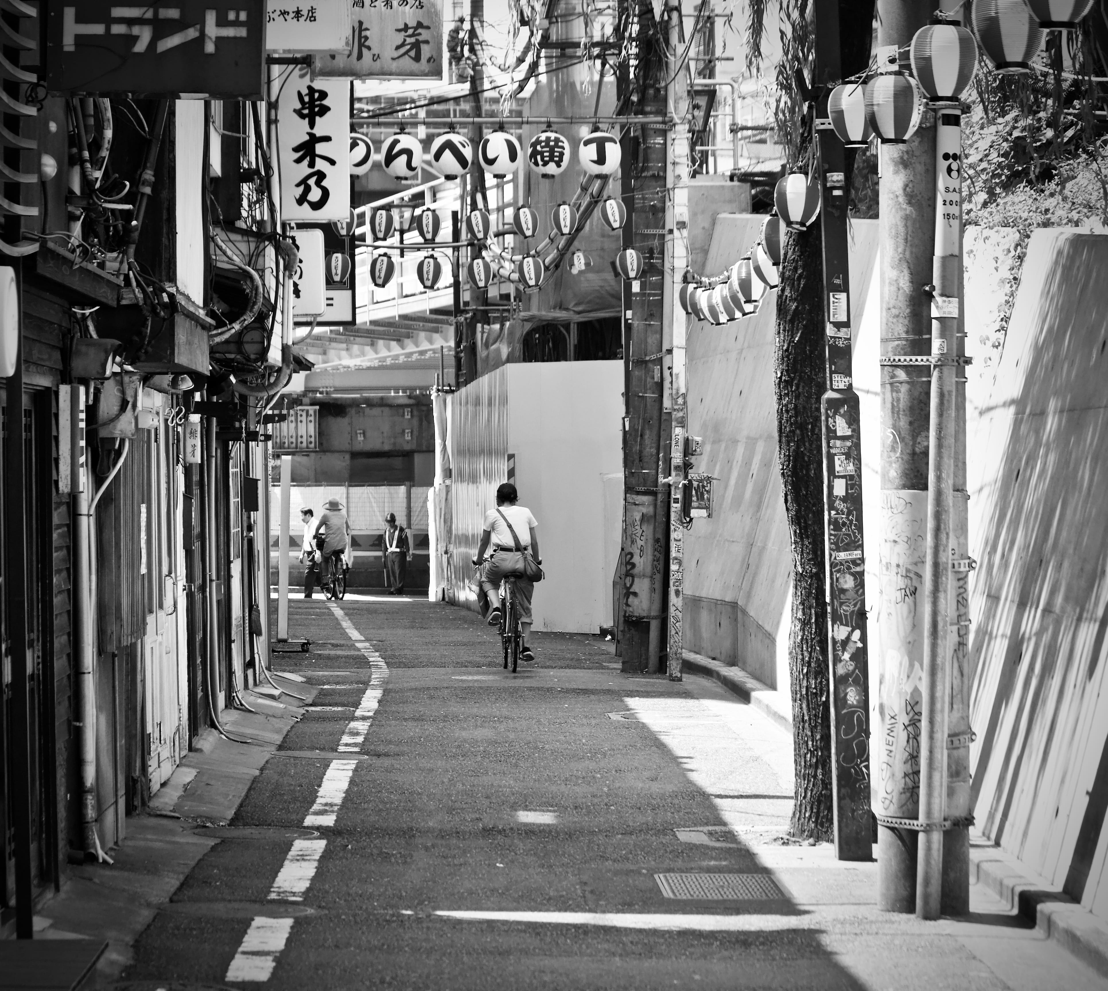 grayscale photo of man riding bike, street, urban, city, alley