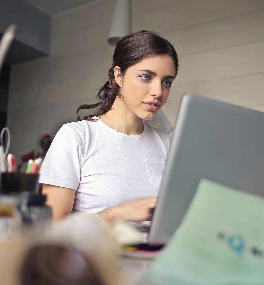 A young brunette woman wearing white T-shirt working on her laptop