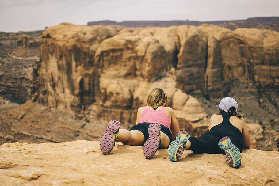 two woman lying face down on top of rock cliff overlooking cliff at daytime, HD wallpaper