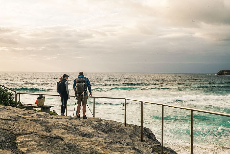 Man and Woman Standing on the Rocky Edge With Hand Rail Beside Ocean HD wallpaper