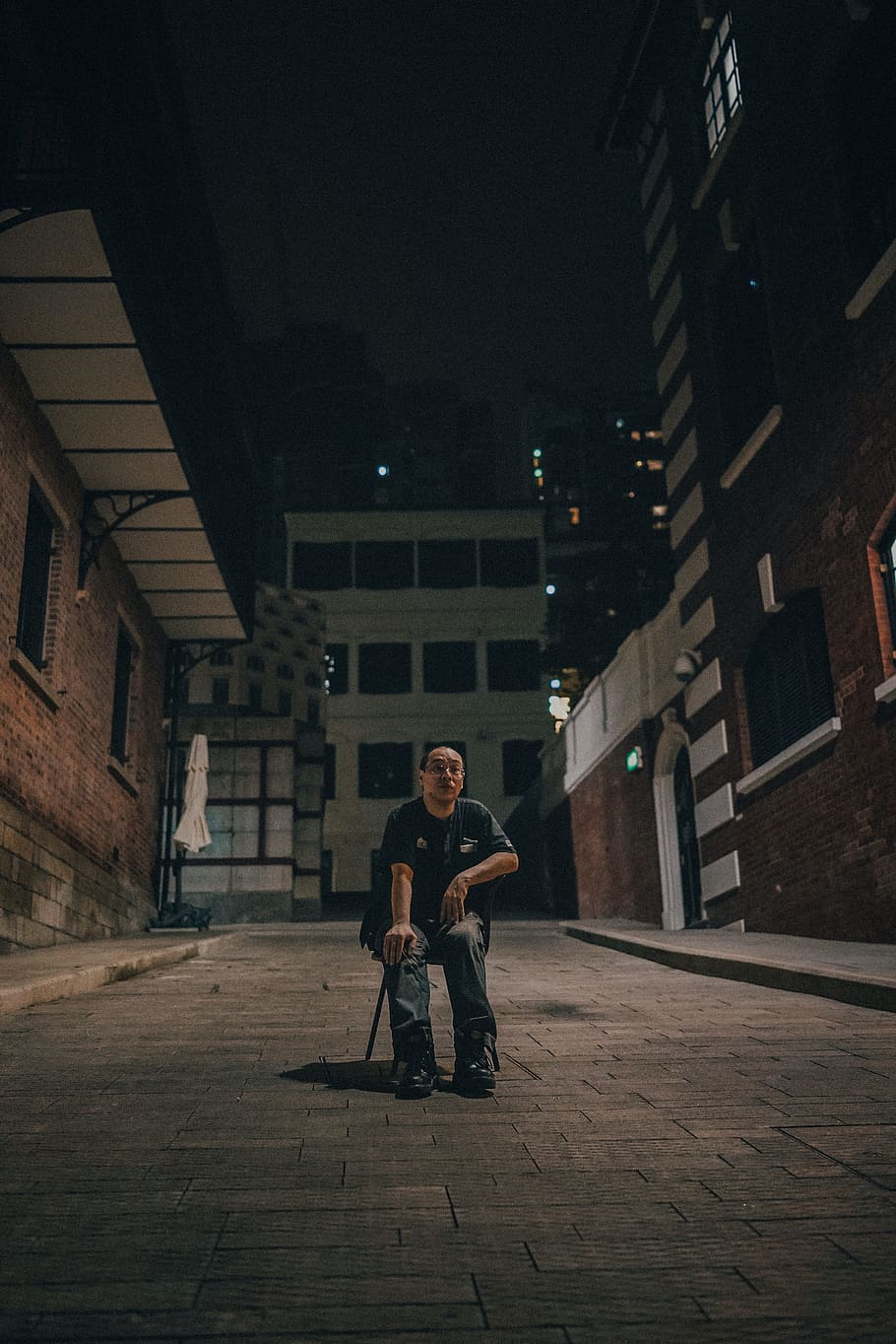 man sitting on chair between brown brick buildings, person, city, HD wallpaper