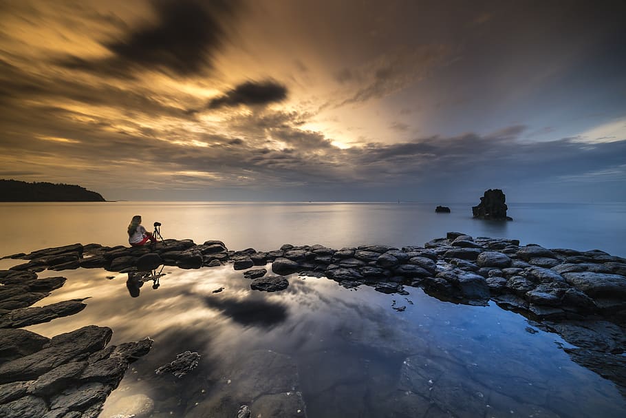 Person Sitting On Stone While Facing The Calm Sea During Sunset HD wallpaper