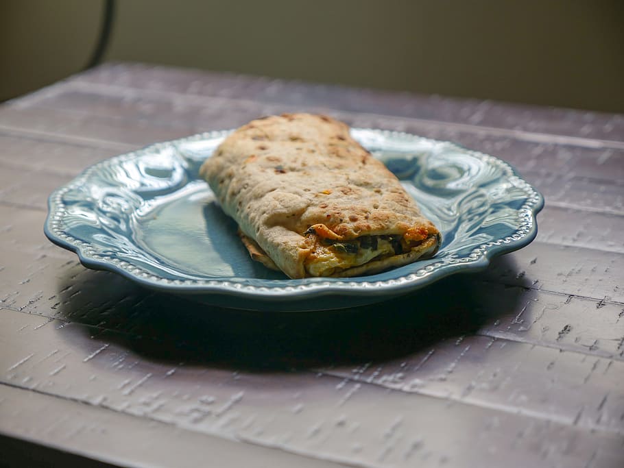 Spinach, feta cheese, and egg all wrapped in a tortilla. Sitting on a blue plate in the sunlight. HD wallpaper