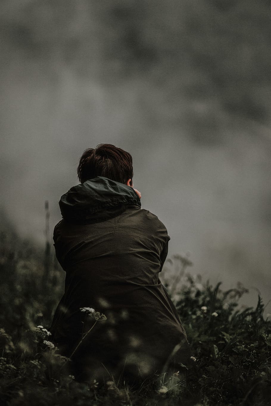 selective focus photo of person in black hooded jacket sitting on green grass field at daytime HD wallpaper