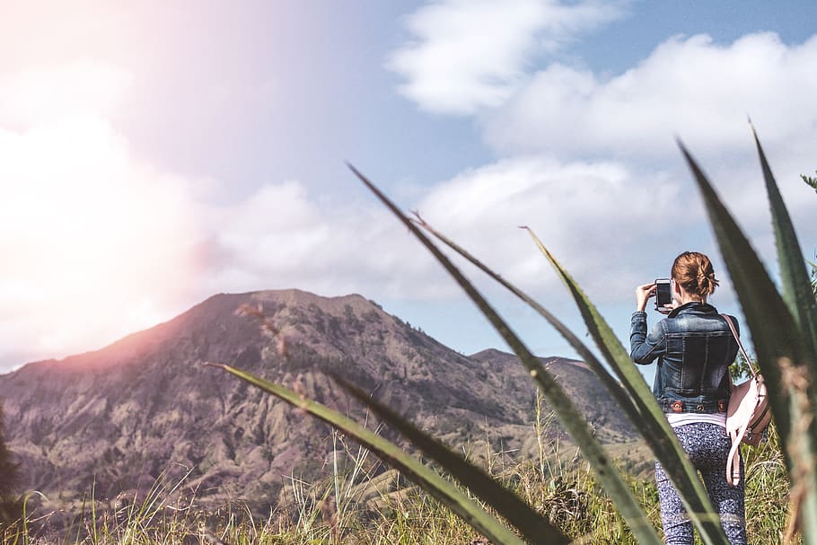 Woman Standing on Green Grass Field Taking Photo of Mountain HD wallpaper