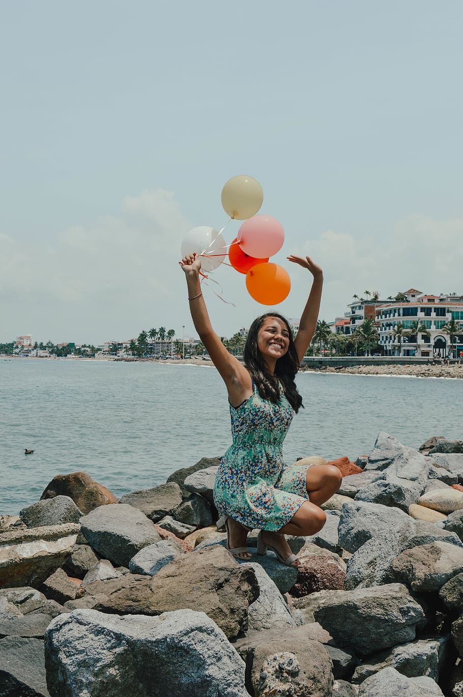 Woman Sitting While Holding Balloons Near Body of Water, afternoon