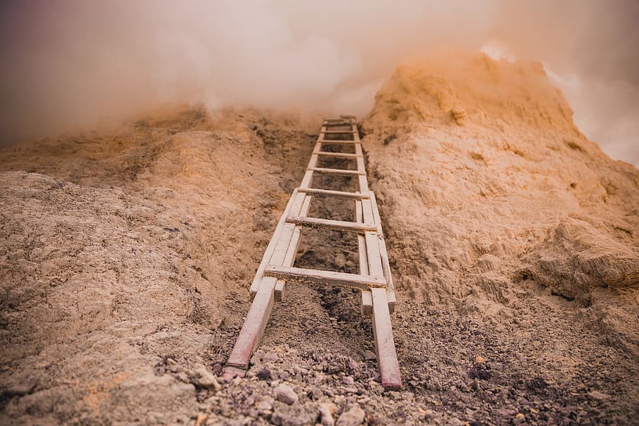 A wooden ladder placed against a rock covered with clouds on an overcast day HD wallpaper