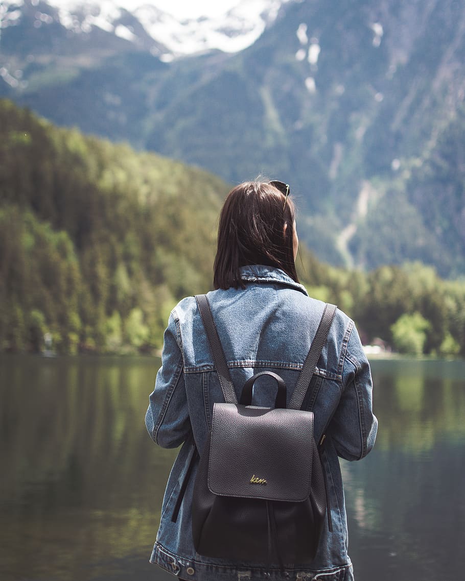 selective focus photography of woman wearing blue denim jacket and black bucket backpack near lagoon at daytime, HD wallpaper