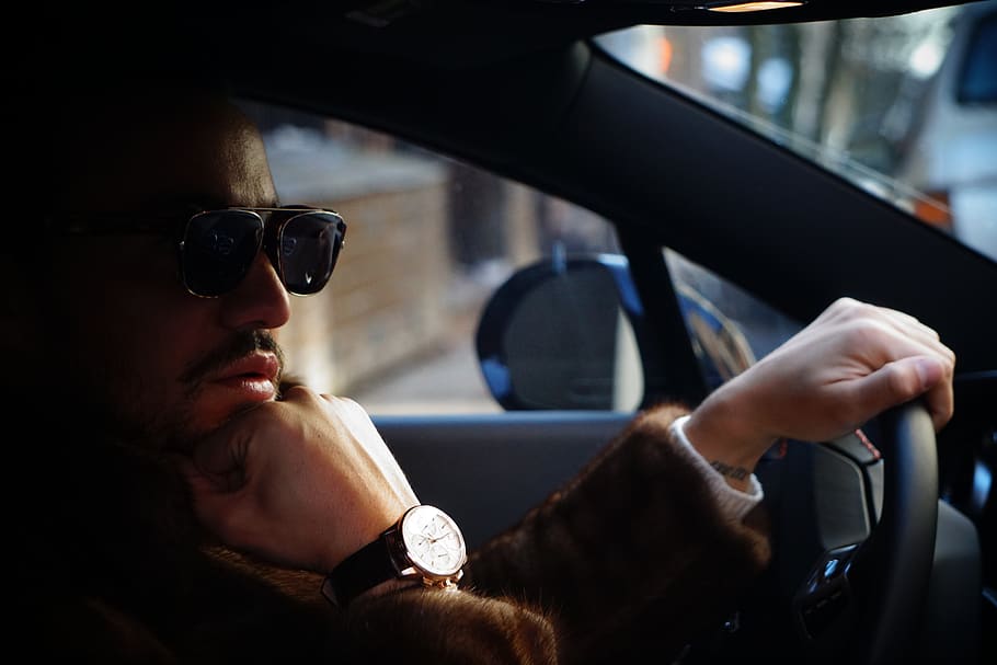 man wearing black sunglasses, gold-colored watch, and brown jacket placing hand on chin inside car, HD wallpaper