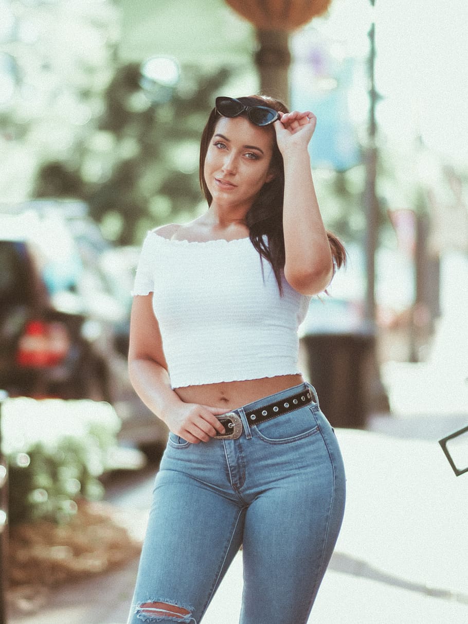 woman in white off shoulder top and blue denim fitted jeans stands near column