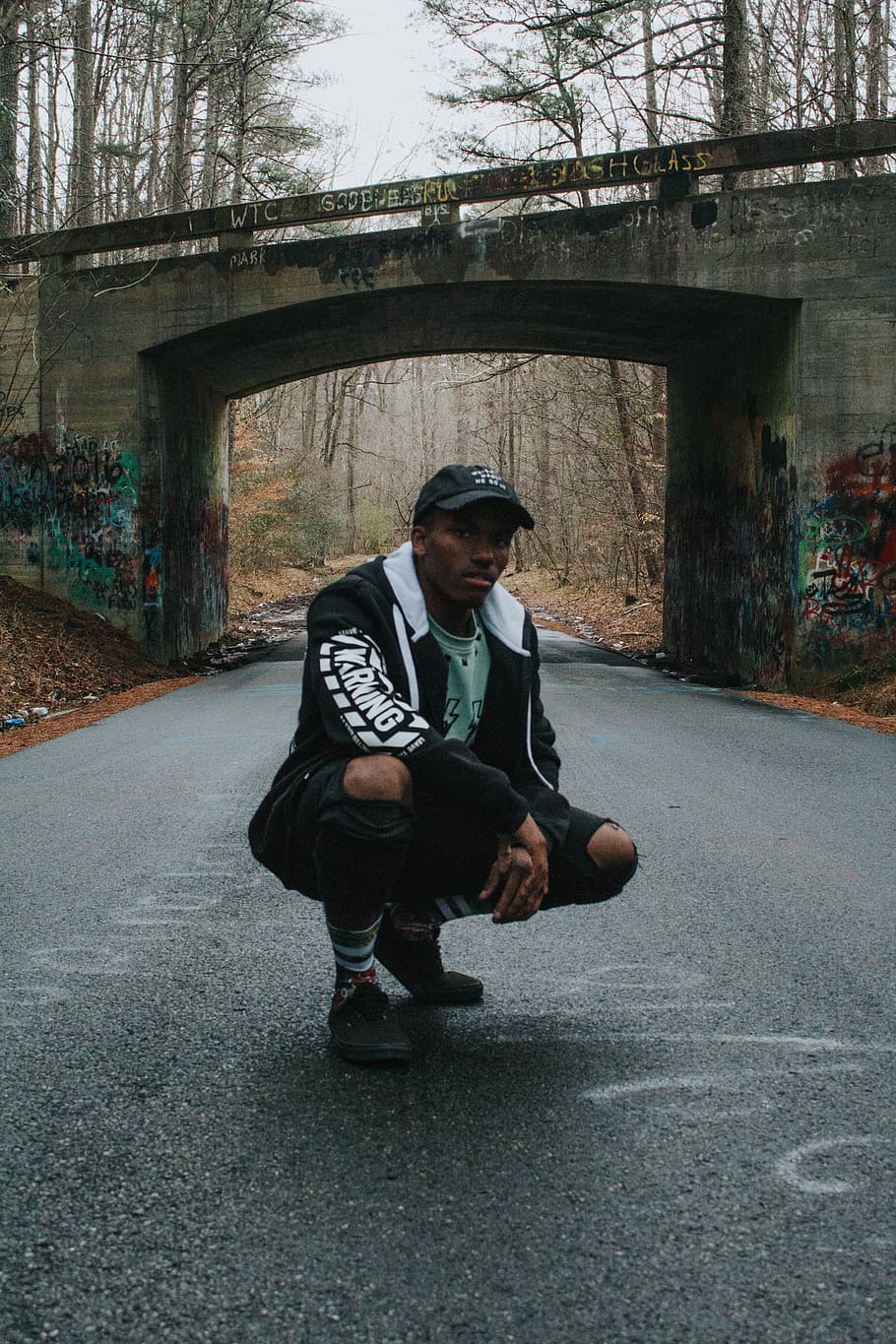 Man Sitting on His Feet on Road, blurred background, bridge, cap