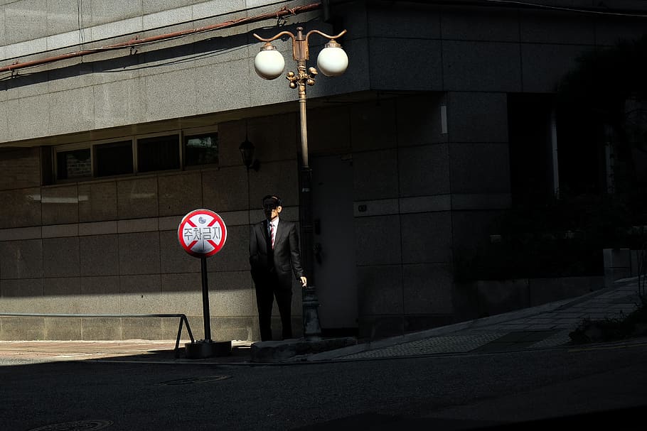 person standing under streetlight by road sign during daytime HD wallpaper