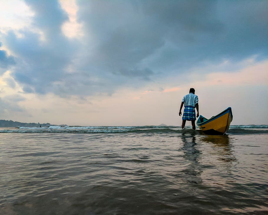 Man on Body of Water Beside Yellow and Blue Boat, beach, clouds HD wallpaper