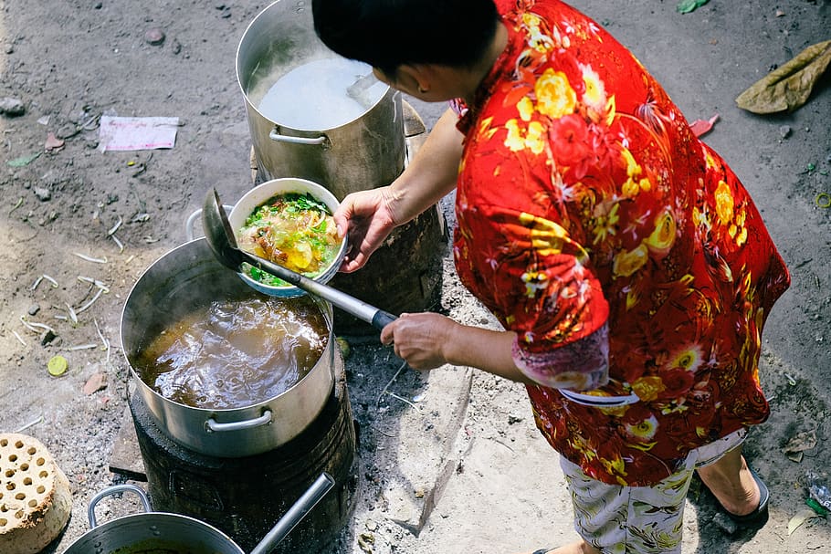 woman in red floral shirt cooking soup outdoors, human, person