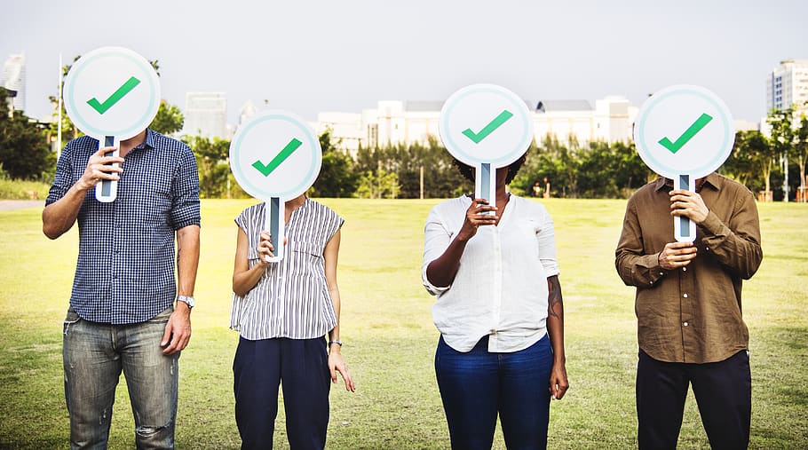 Four People Holding Green Check Signs Standing on the Field Photography