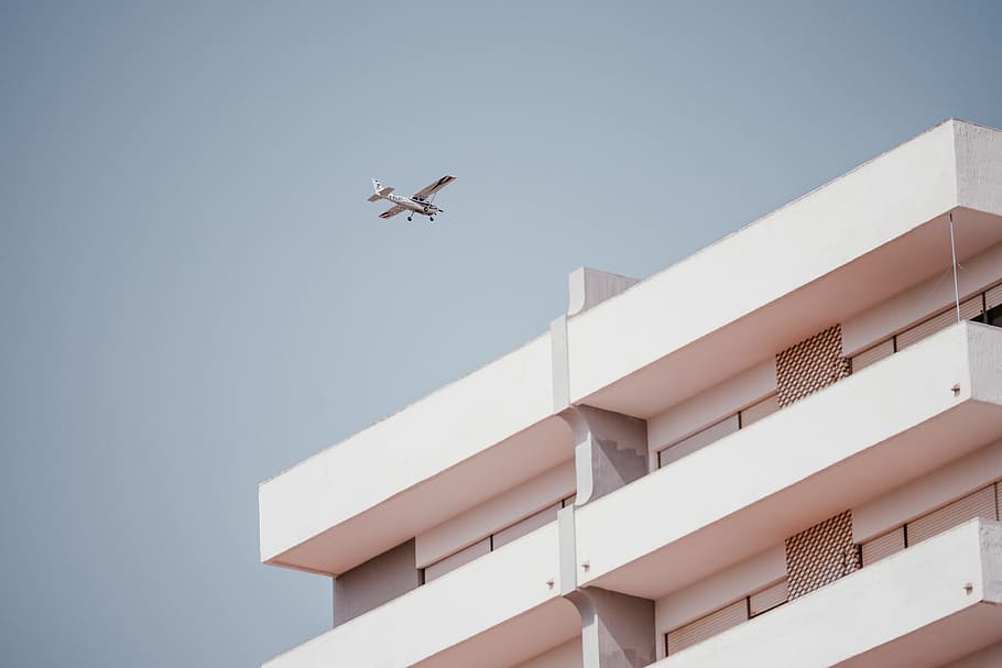 white monoplane passing thru building, airplane, aircraft, wing