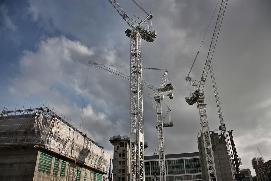 View of Cranes working on a construction site, with dark clouds seen in the sky HD wallpaper