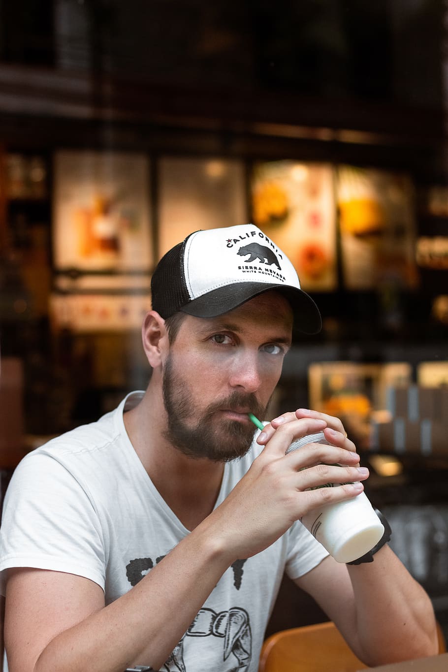 Man Sipping Straw, beverage, blurred background, cap, casual