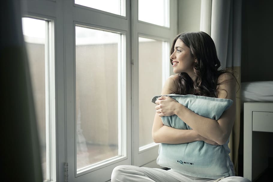 A young brunette woman looks outside the window while emracing a pillow, HD wallpaper