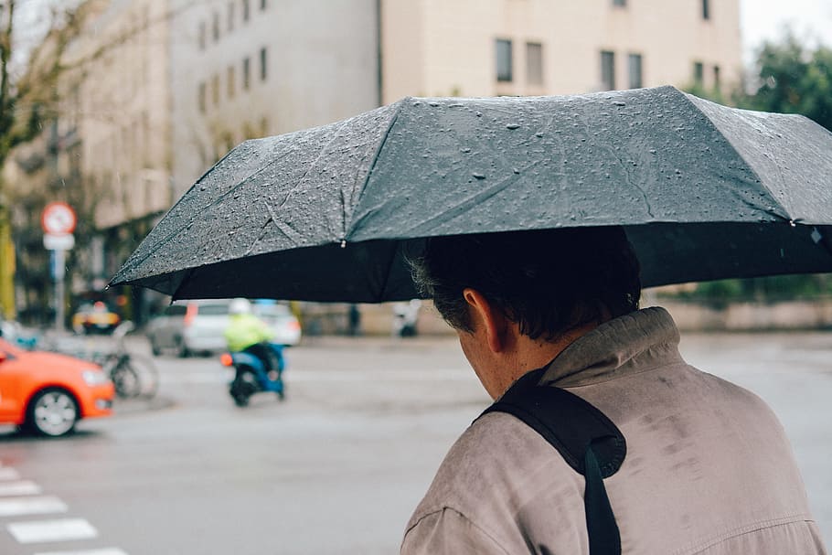 Man Holding Black Folding Umbrella Walking Along Street, architecture