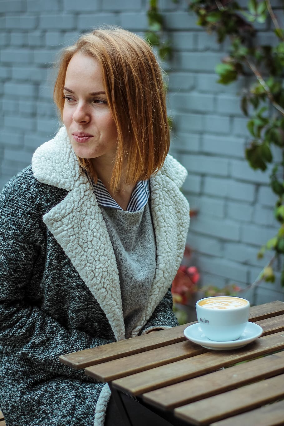 Woman Wearing Gray Coat in Front of Brown Table With White Coffee Cup