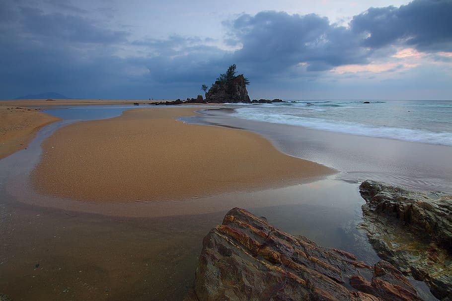 Sea Wave Crashing on Seashore With View of Rock Formation With Trees on Top of It Under Grey Clouds and White Sky HD wallpaper