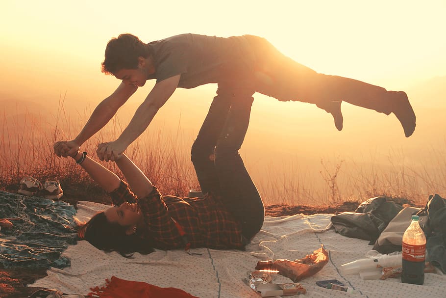 Woman Lying on Blanket Under Man on Her Legs Holding Hands during Golden Hour HD wallpaper