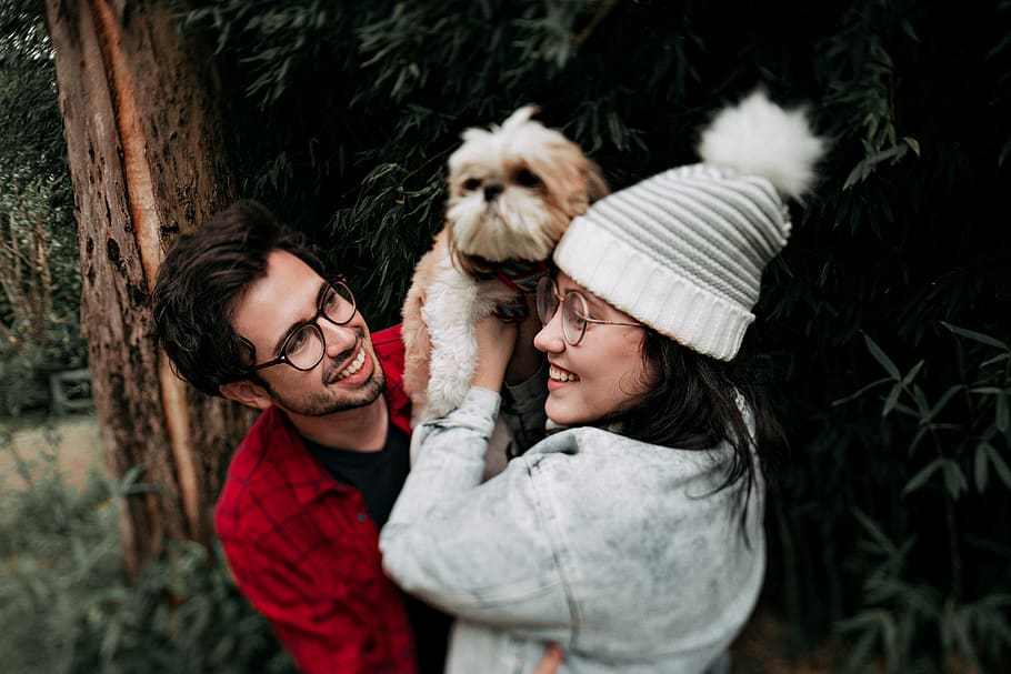 Woman Lifting Puppy in Front of Man Near Tree, 20-25 year old