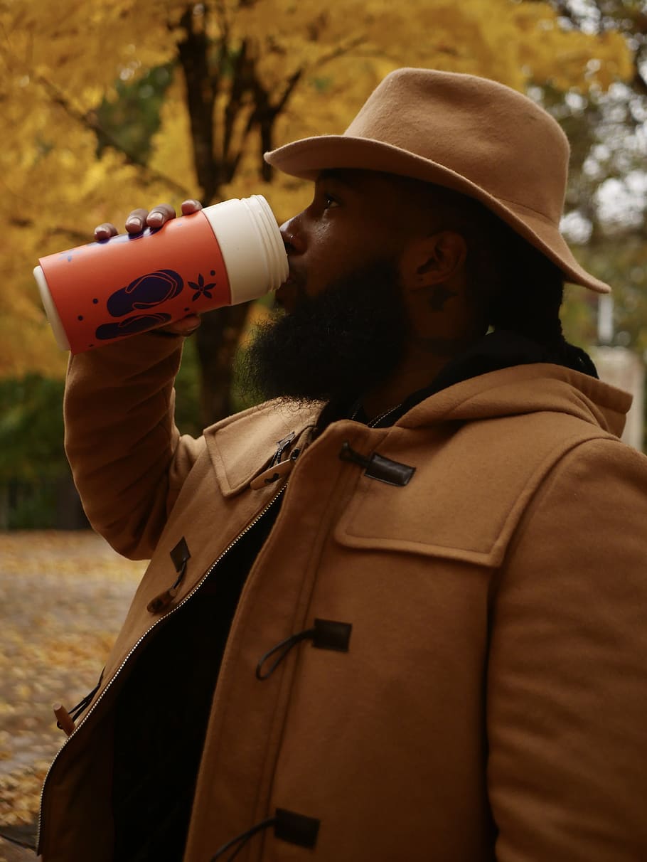 Photo of Man in Brown Hat and Brown Outerwear Drinking from Plastic Tumbler