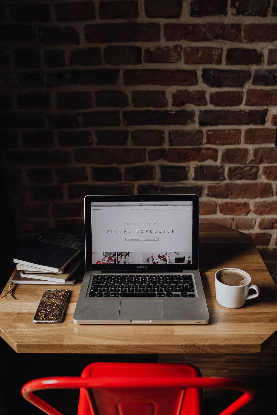 Creatives desk with laptop, camera, journals and books in front of brick wall HD wallpaper