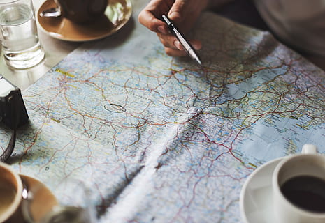 Person Holding Pen Leaning on Map Near Cup, activity, adventure HD wallpaper
