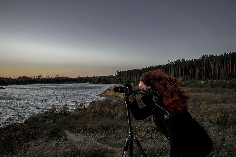 Woman in Black Coat Holding Dslr Camera With Stand Near Body of Water HD wallpaper