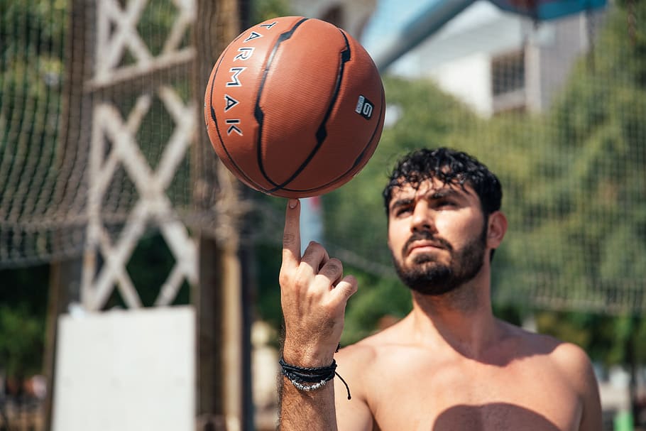 A young man spinning basketball on his finger in sunlight, 20-25 year old