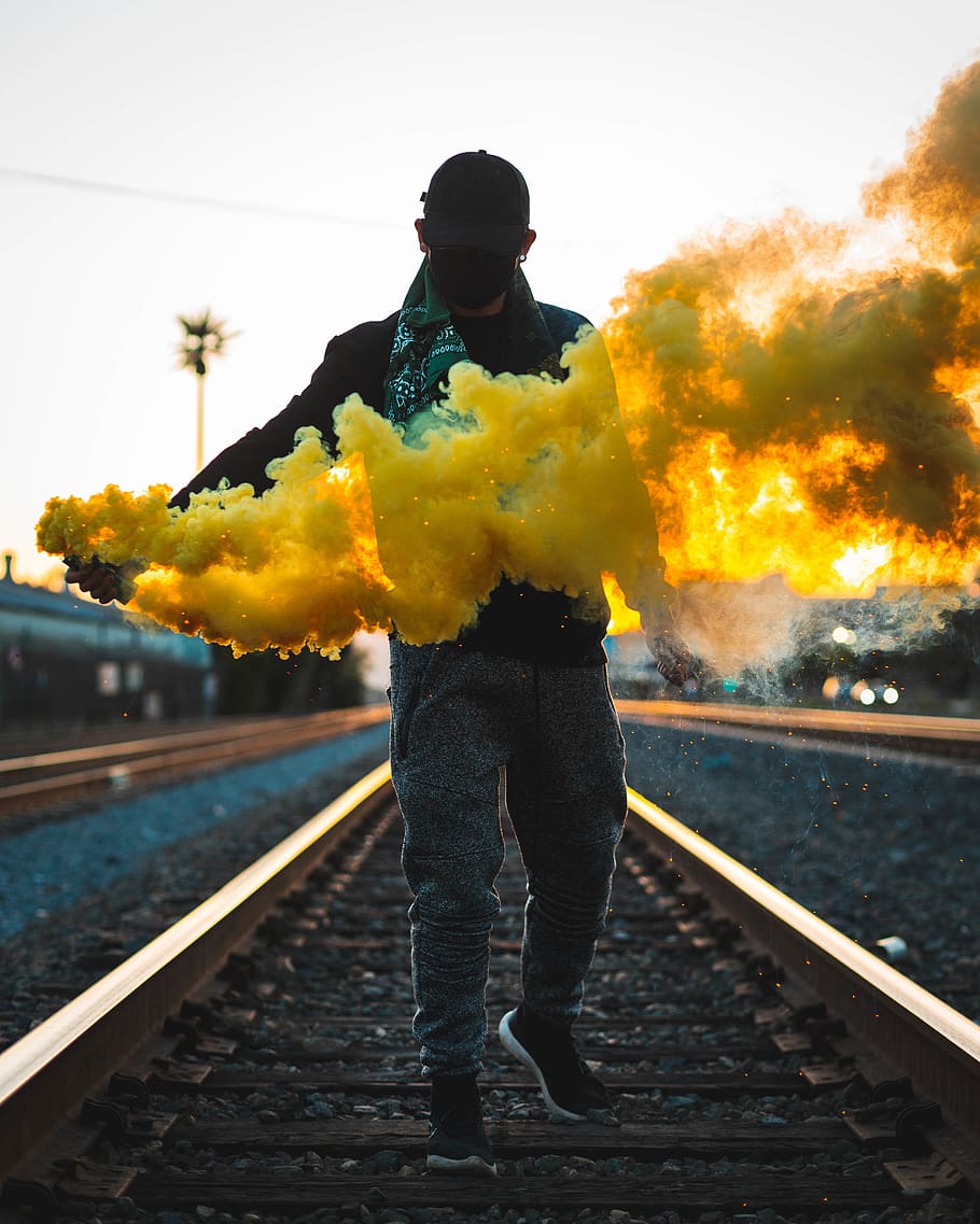Photo of Man Standing on Train Tracks Holding a Yellow Smoke Bomb